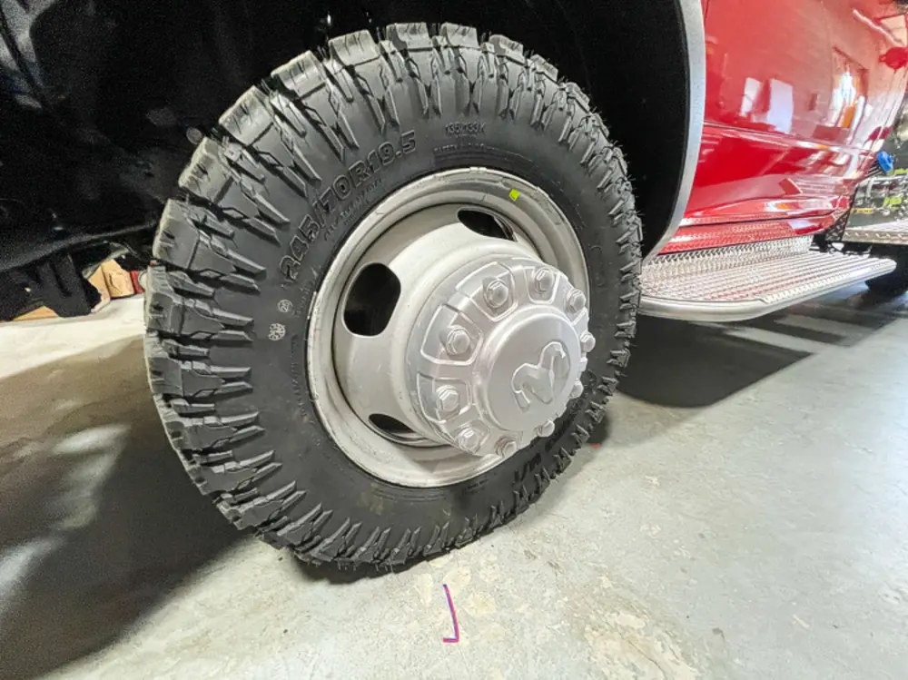 Exterior view of small fire truck showing cab, body compartments, and wheel/tire area.